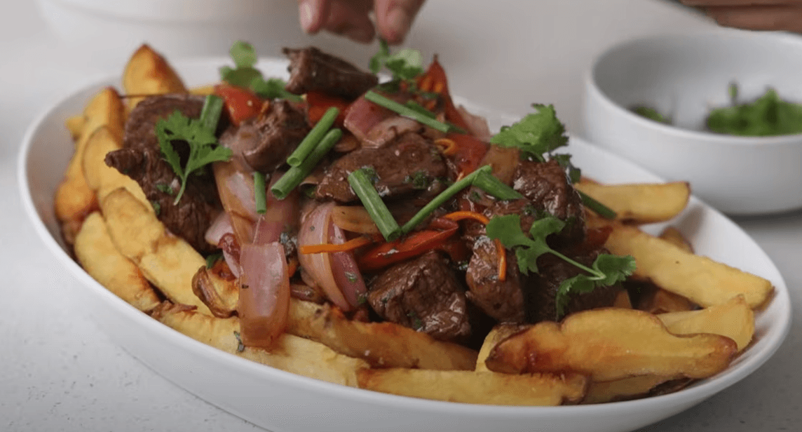Plato de Lomo Saltado servido sobre papas fritas con arroz con choclo al lado.