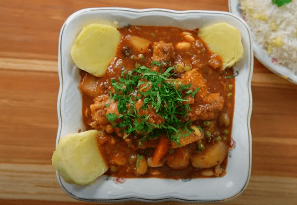 Plato de estofado de pollo criollo servido en plato hondo con arroz con choclo al lado.